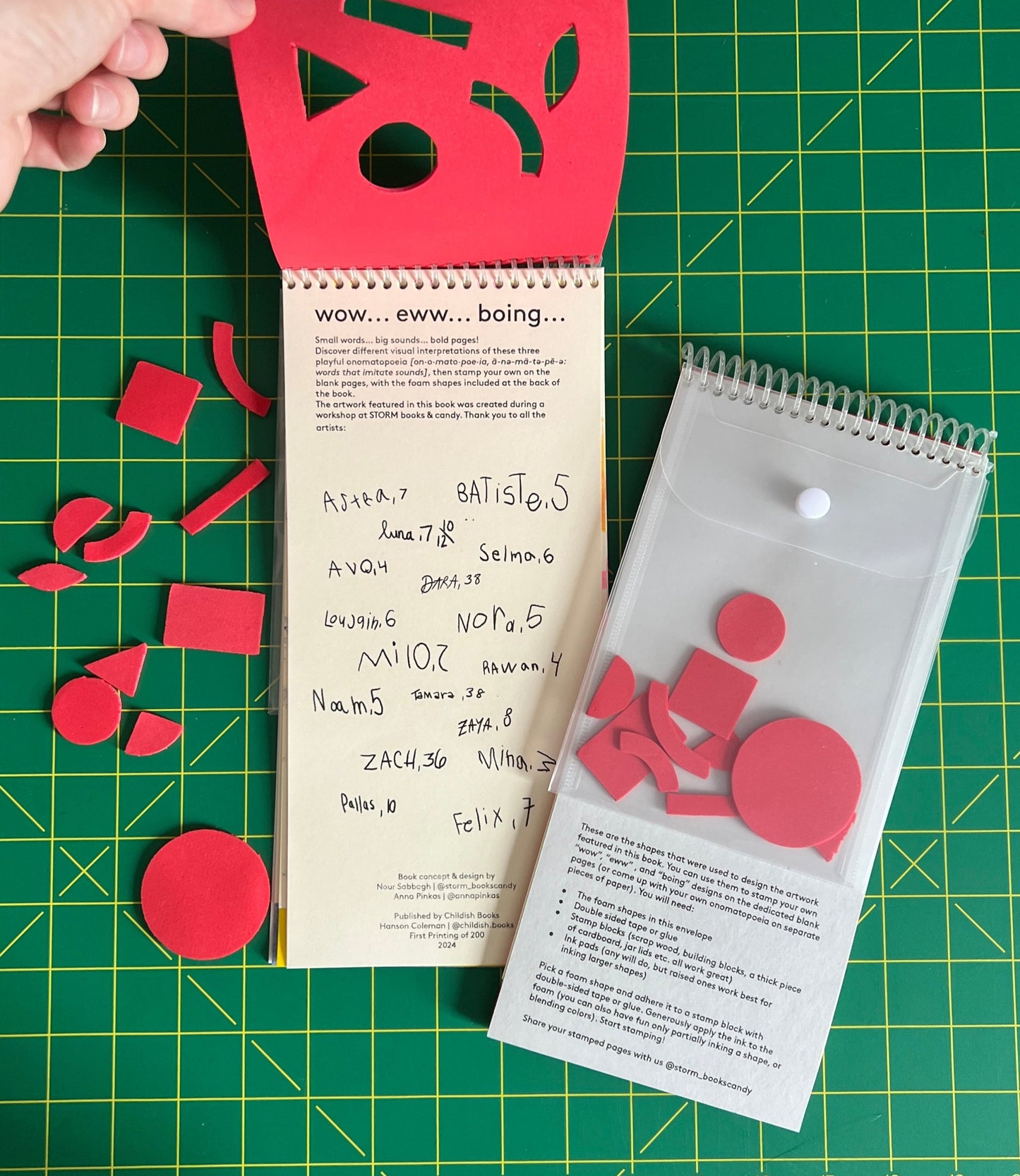 Hanson’s hand peels up the vertically coil bound foam cover to fully reveal the books title page. A second copy is flipped over to display the back cover, featuring a clear plastic envelope which contains a set of dicut foam cut out shapes (the inverse of the cover) behind it stamped making instructions are printed onto a gray card stock.